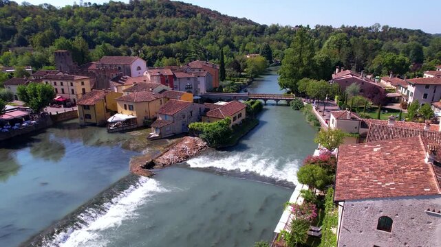 Italy Borghetto sul Mincio 4K Static Drone Video of Medieval Village with Colorful Houses in Middle of River and Flowing Waterfalls Near Lake Garda Scenic Still Aerial View
