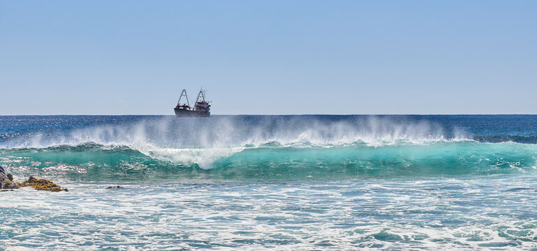 Brechende Wellen an der K&uuml;ste der Galapagos-Inseln mit Schiff am Horizont