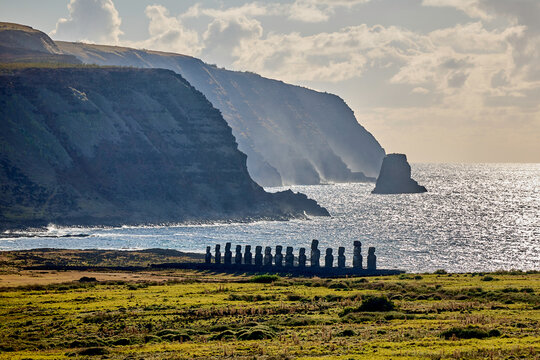 Die 15 Moai von Ahu Tongariki an der K&uuml;ste der Osterinsel vor steilen Klippen.