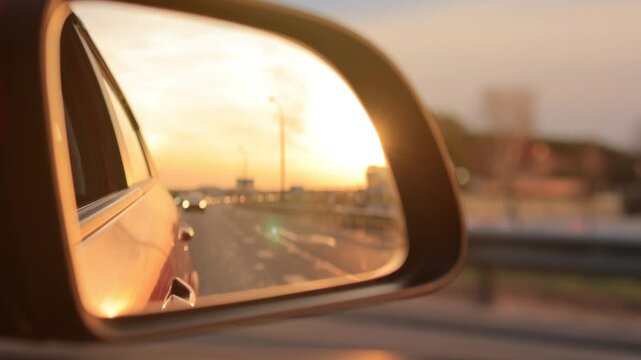 The sun is reflected in the mirror, evening road. View in the side rear view mirror of a red car driving along the highway