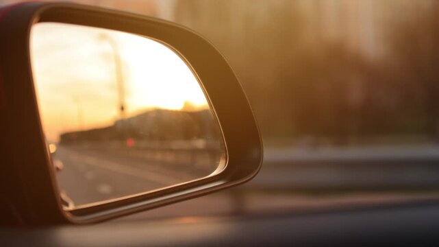 The sun is reflected in the mirror, evening road. View in the side rear view mirror of a red car driving along the highway