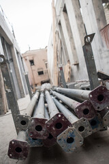 Sturdy steel props are neatly stacked on the ground at a construction site. Surrounding frames rise high, showcasing the busy progress of building in an urban setting
