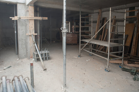 Inside a spacious construction site, scaffolding towers rise as workers meticulously set up frames and beams for a new structure. Dust swirls in the air, hinting at hard work