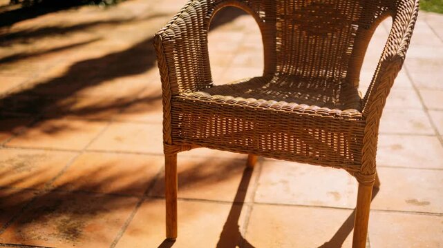 Camera tightening view on rattan chair centering on terracotta patio, showing woven seat and shadow