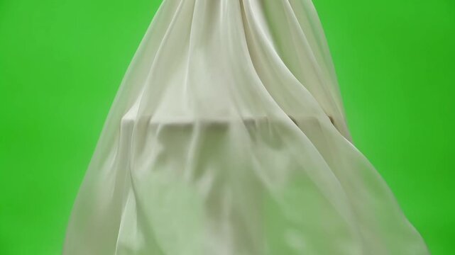 A close-up shot of a white fabric draped elegantly against a vibrant green background with folds and creases visible.