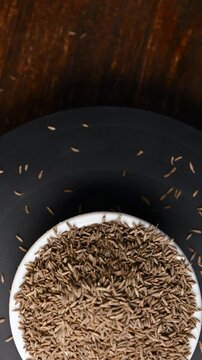 Top View of Cumin Seeds (Jeera) in White Bowl on Black Background &ndash; Rotating Vertical Footage