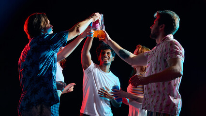 Naklejka premium Friends clinking bottles and cans celebrating party moment in dark studio. Concept of celebration campaigns, beverage advertising, friendship moments and lifestyle branding.