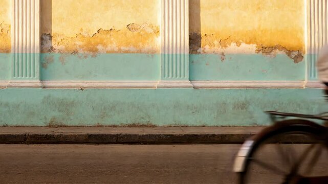 Adult male pedaling bike, entering left and riding past painted wall, motion line for urban design