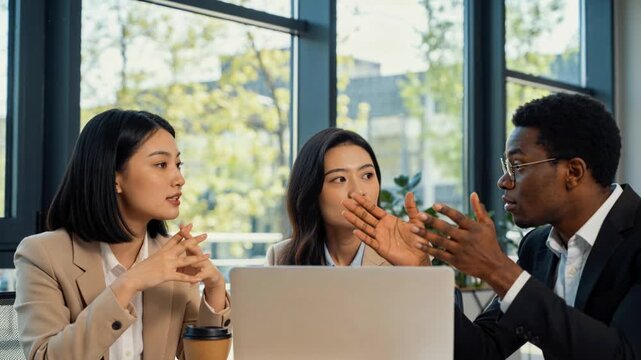 Explaining left woman in beige blazer clarifying points at table while right man pointing at laptop