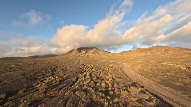 Aerial view of sunset over desert and mountains in background. Drone point of view, flying low over dirt road, cinematic birds eye view.