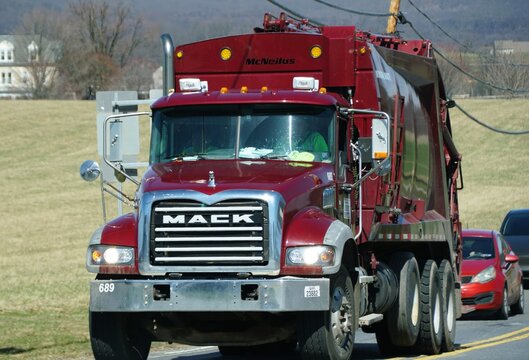 Downingtown, Pennsylvania, U.S - March 21, 2026 - A red McNeilus Mack heavy-duty garbage truck traveling on rural road with fields and trees