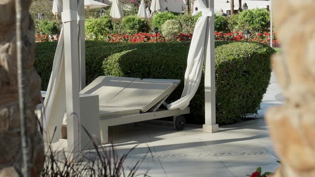 Detail of a comfortable sun lounger with a folded white umbrella next to a green manicured hedge. Quiet relaxation spot in a high-end Egyptian hotel during summer season.
