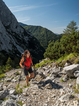Hiking, lifestyle: Woman hiking uphill with poles on a rocky trail, surrounded by mountains and trees, concept for outdoor adventure. Volaia lake, Italian-Austrian border, Friuli Venezia Giulia