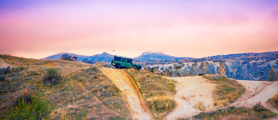 Off-road green SUV, 4x4 driving on a dirt ridge in a vast desert canyon landscape at sunset. © M.studio