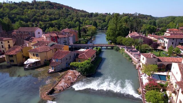 Aerial view of Borghetto sul Mincio, one of Italy's most beautiful villages. Panning shot of medieval watermills, waterfalls on Mincio river and authentic Italian borgo architecture. 4k drone