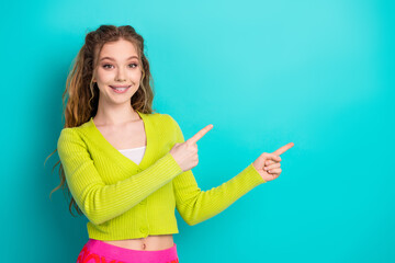Obraz premium Cheerful young woman pointing energetically against a bright turquoise background in casual attire conveying happiness and positivity