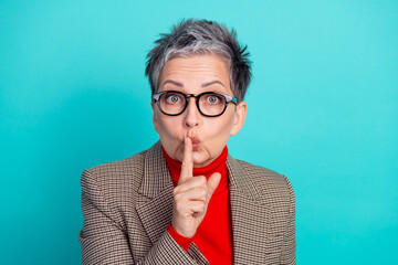 Shh a stylish senior businesswoman in a check blazer and red turtleneck poses playfully against a...