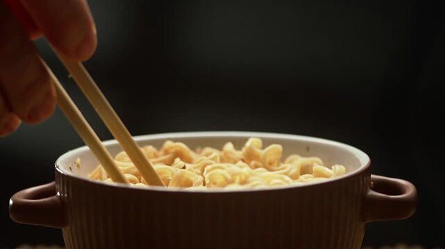 Eating instant noodles with chopsticks from bowl with smoke on black background. Healthy eating concept