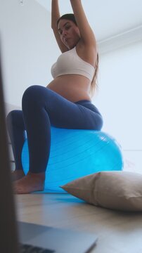 Expectant mother doing prenatal fitness exercises on a stability ball while watching her laptop