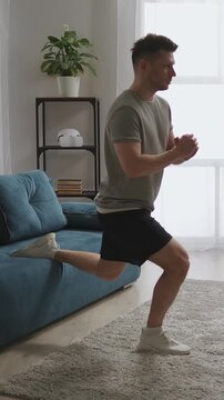 Focused man performing Bulgarian split squat exercise at home using sofa support, demonstrating single-leg strength training, balance, and stability in bright living room