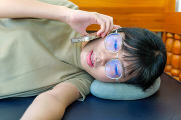 Naklejka premium young Asian woman lying down using smartphone with blue light glasses and neck pillow