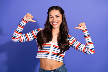 Young female model wearing a striped crop top poses with arms raised against a violet background...