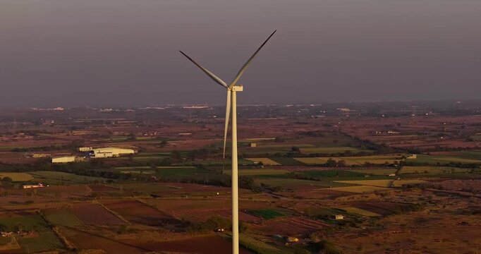 Golden hour aerial view of wind turbines across rural farmland, with rotating blades under a warm orange sky, showcasing clean energy and a serene countryside landscape of Gujrat, India