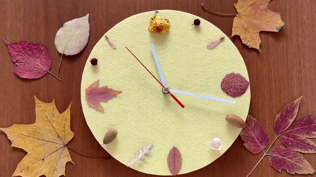 Time of autumn. Video of handmade clock with a yellow dial, with fallen leaves instead of numbers, on wooden background. Concept for the arrival of autumn season