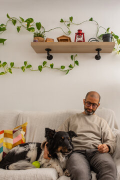 Adult man hugging dog on couch looking with affection at home cozy scene
