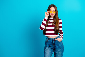 Young woman in striped crop top and jeans wearing yellow sunglasses posing confidently against...