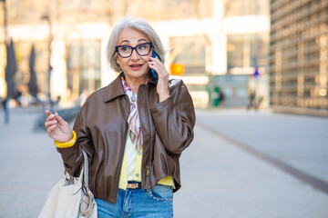 Fototapeta premium Senior woman talking on phone and gesturing in city