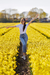 Fototapeta premium Happy woman with arms outstretched in yellow daffodil field, sunny spring day in the Netherlands
