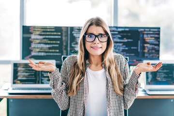 Female programmer shrugging in front of multiple monitors with code, confused developer reaction...