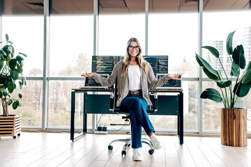 Young female software developer smiling in a modern office workspace with dual monitors showing...