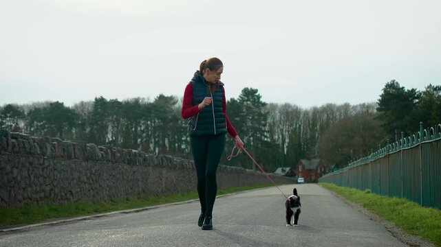 Sporty woman running alongside pet cat on quiet road. Training with companion animal combining cardio exercise and pet care. Healthy routine strengthening bond between owner and domestic pet