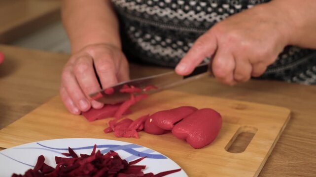 Shredding red pepper into thin strips for Ukrainian borscht. Cutting sweet pod vegetable creating garnish for national soup of Ukraine. Slicing fresh capsicum preparing colorful base for traditional