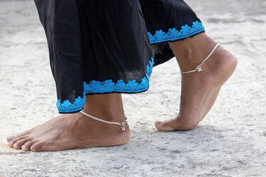 Close-up of a woman walking barefoot on a textured concrete surface, wearing traditional silver anklets or payal with intricate bell details