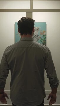 Vertical video: Walking man heading down home hall to view frosted glass and floral art, shirt