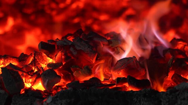 Burning charcoal surface with bright embers and dark texture creating a powerful abstract fire background.
