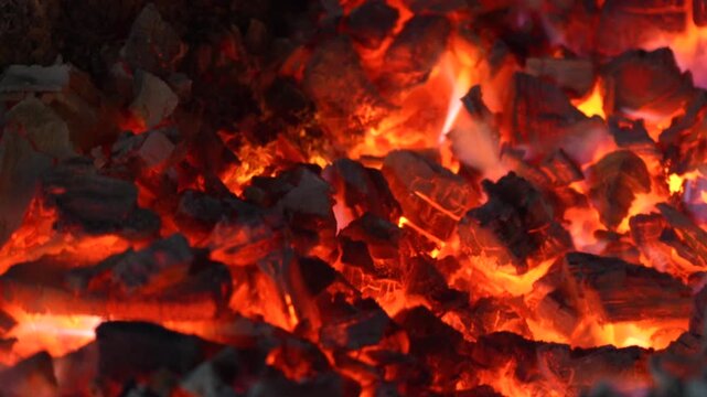 Burning charcoal surface with bright embers and dark texture creating a powerful abstract fire background.