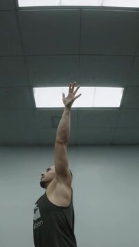 Man shifting weight forward and lifting arm for hip stretch under ceiling light on fitness mat