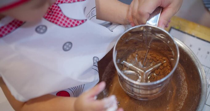 Child sifting cocoa powder into a mixing bowl at a home kitchen counter, promoting hands-on culinary skill development and family bonding through baking activities.