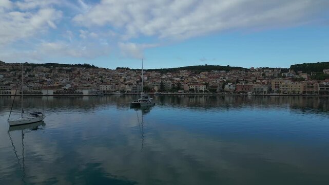 A charming Greek town rises from a hillside overlooking a calm harbor dotted with sailboats.