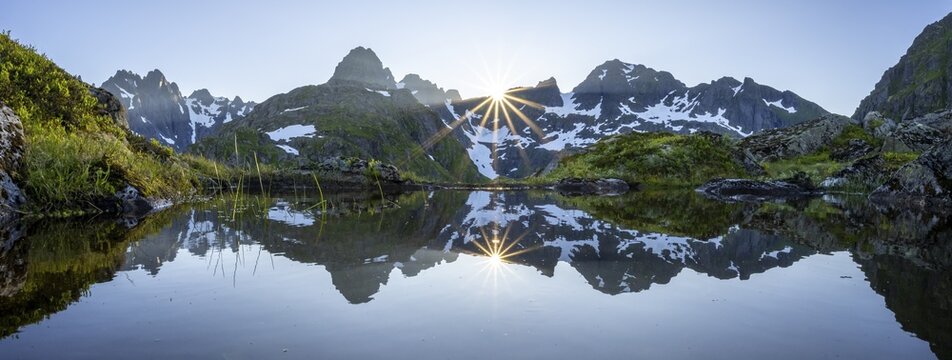 Mountain panorama, high moor, mountains reflected in a pond, sun shining over mountains with snow, at the Trollfjord Hytta, at the Trollfjord, Lofoten, Nordland, Norway