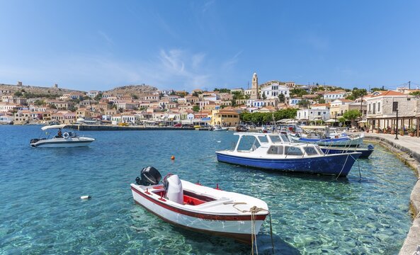 Fishing boats in the harbour of Halki with turquoise water, promenade with colourful houses of the village of Halki, Halki, Dodecanese, Greece
