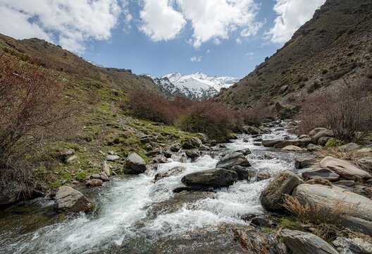 Mountain stream Rio Valdeinfierno, hiking trail near Junta de los Rios, behind Sierra Nevada with summits Mulhac&eacute;n and La Alcazaba, snow-covered mountains near Granada, Andalusia, Spain