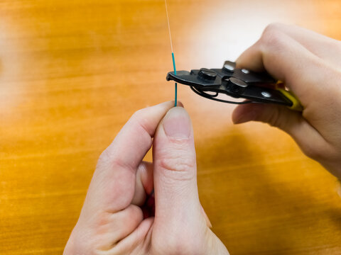 Professional technician hands stripping fiber optic cable with special tool on wooden background. Process of cleaning optical fiber for internet connection, data transmission, and network installation