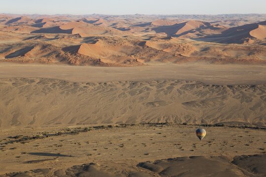 Hot-air balloon above an arid plain and the dry riverbed of the Tsauchab river at the edge of the Namib Desert, photographed from a second balloon, Namib-Naukluft National Park, Namibia