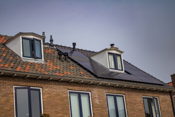 Obraz premium Brick residential houses with red tile roofs featuring rooftop solar panels on a sunny day, showcasing sustainable and energy-efficient home design.. High quality photo