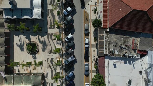 Aerial view of a street lined with cars and buildings, featuring palm trees and unique architectural elements.